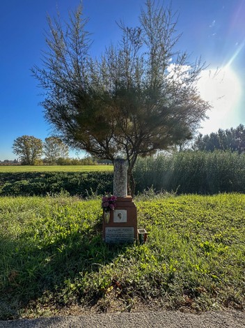 Cippo a Gasparini con albero ornamentale e decorazioni floreali in un paesaggio rurale.
