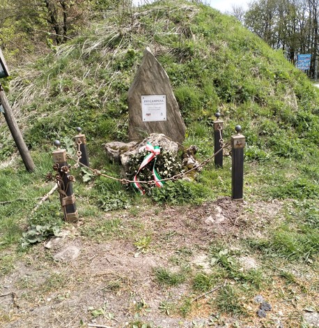 Cippo a Campana circondato da elementi naturali e decorato con nastri tricolori e legature.