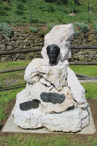 Monumento a Locatelli, con busto in bronzo sorretto da una base di pietra, immerso in un contesto verde.