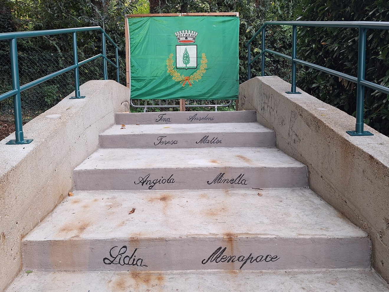 Scalinata in pietra con nomi incisi su ogni gradino, bandiera verde con stemma sul pianerottolo superiore.