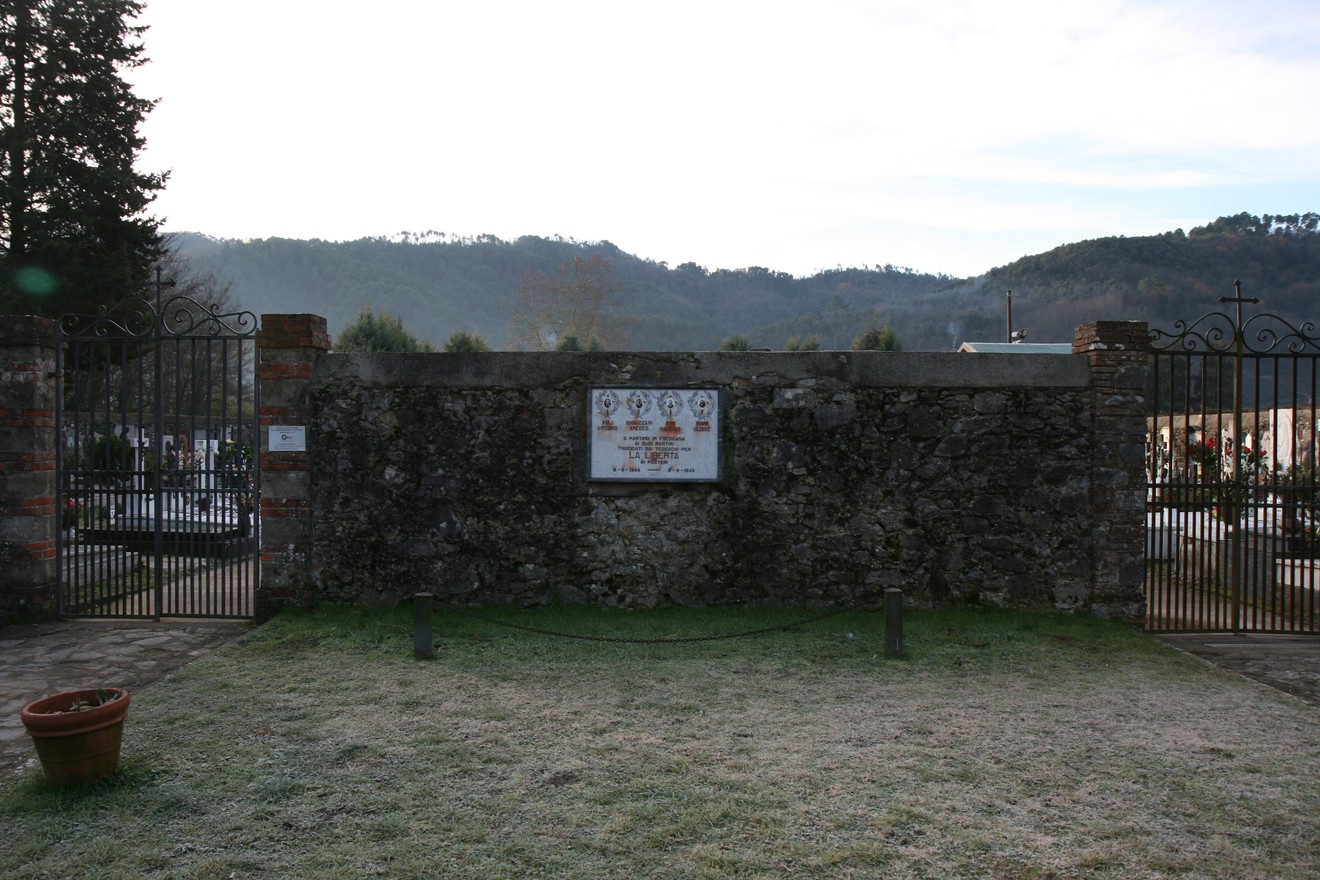 Lapide all'ingresso del cimitero di San Martino, circondato da un paesaggio montano.