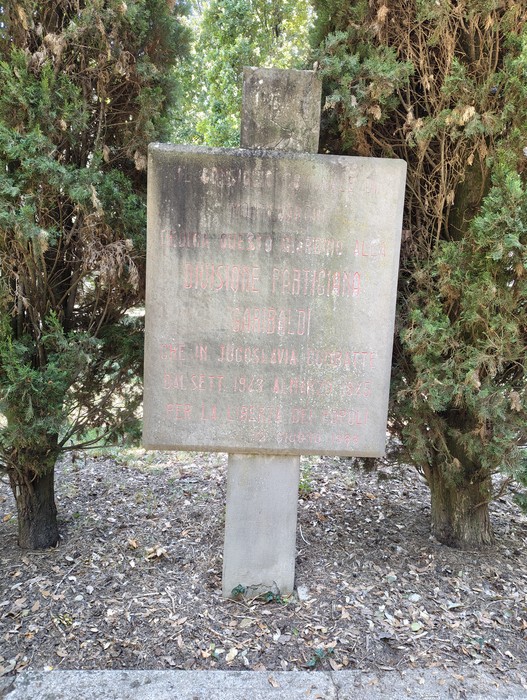 Stele in pietra con iscrizione consumata, sormontata da una croce, tra due alberi di cipresso.
