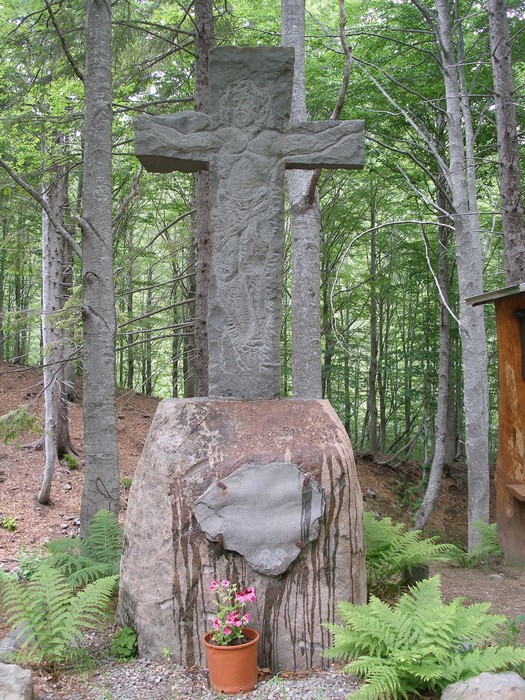 Croce di Lago Nero, monumento in pietra immerso nel verde del bosco, circondato da alberi e piante.