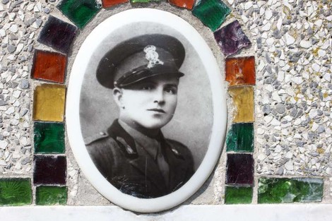 Un cippo dedicato a un militare, con una fotografia in bianco e nero incastonata in una decorazione colorata.