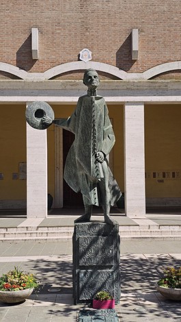 Monumento a Minzoni, scultura in bronzo raffigurante un personaggio con un cappello, situato in un contesto architettonico.