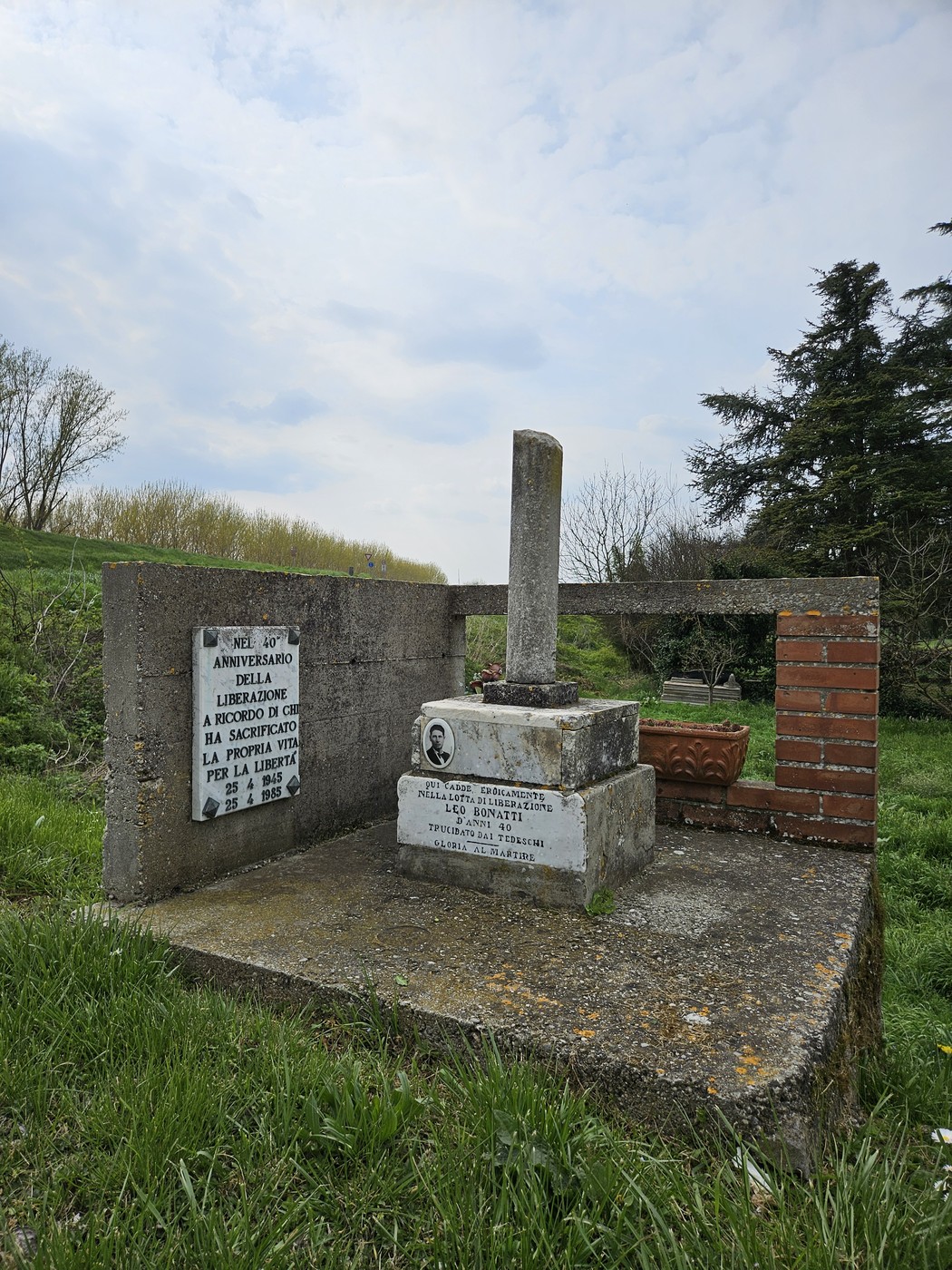 Cippo commemorativo in un'area verde, caratterizzato da un obelisco e decorazioni floreali.
