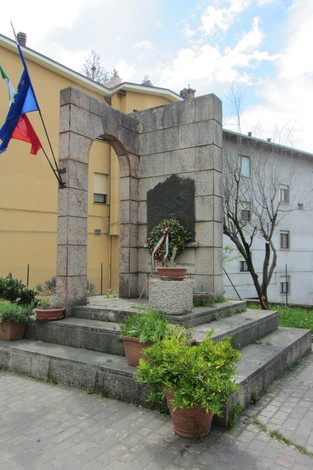 Monumento ai caduti della Resistenza, con altare e lapide, circondato da piante e bandiere.
