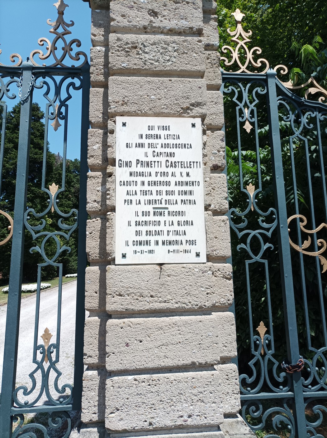 Lapide commemorativa dedicata a Gino Prinetti Castelletti, posta su una recinzione in pietra.