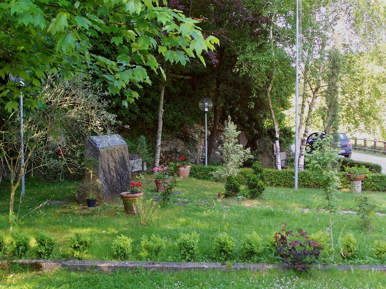 Area monumentale dedicata ai Caduti di Partina, immersa nel verde, con piante e fiori commemorativi.