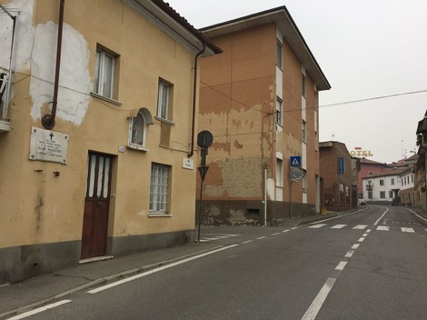 Una visione della strada a Palestro, con un edificio storico e la lapide commemorativa visibile su un muro.