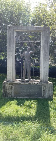 Monumento ai deportati, raffigurante una figura umana in una struttura di metallo, immerso nel verde circondato dalla natura.