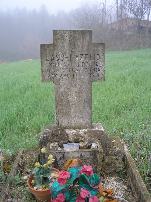 Cippo commemorativo dedicato a Laschi Azelio, situato in un paesaggio verde e nebbioso.
