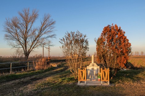 Cippo commemorativo immerso nel paesaggio, circondato da alberi e vegetazione. Atmosfera serena e suggestiva.
