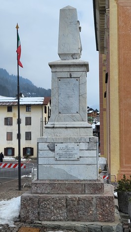 Monumento ai Caduti di Sappada, una struttura in marmo con lati decorati, situato in un contesto montano.