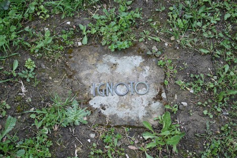 Monumento nel cimitero di Stia, dedicato a un individuo ignoto, circondato da erba e natura.