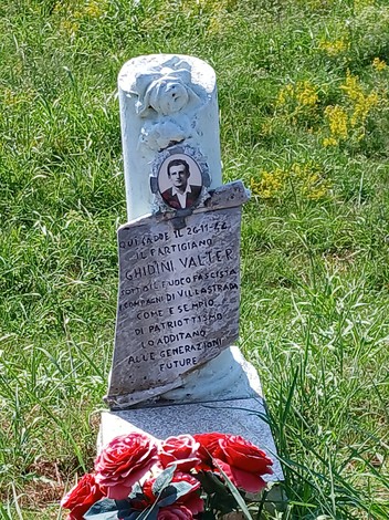 Cippo commemorativo a Ghidini in onore di Valter Ghidini, artigiano e patriota. Decorato con fiori e foto.