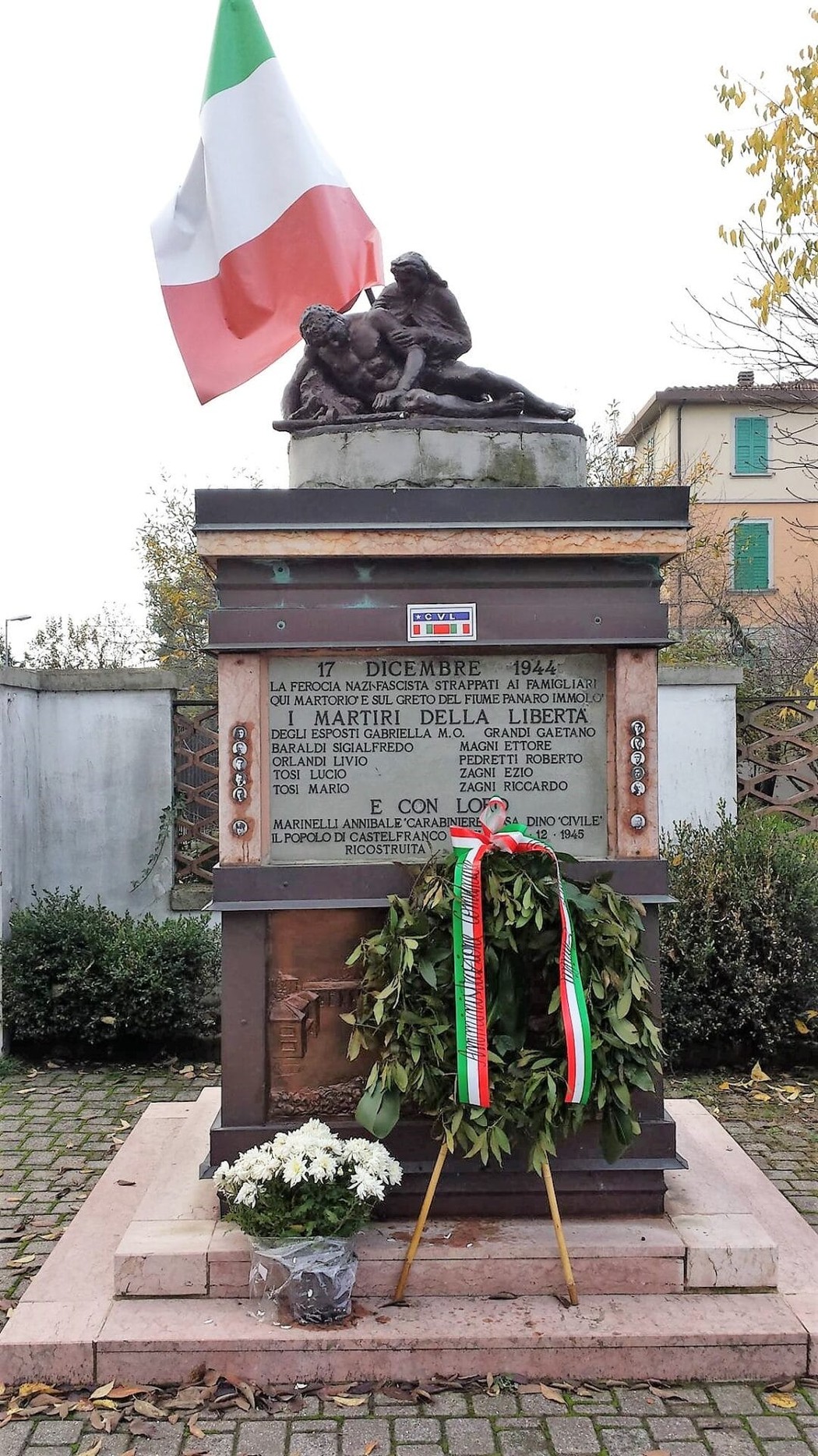 Monumento ai Martiri del Panaro, con bandiera italiana, decorazioni floreali e iscrizioni commemorative.