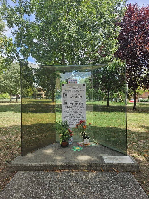 Monumento ad Anderlini e Paltrinieri, situato in un parco, con piante e fiori attorno.