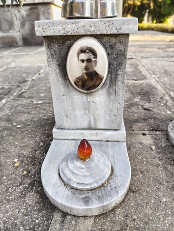 Monumento commemorativo con una foto in bianco e nero e un oggetto rosso in cima, dedicato ai caduti.