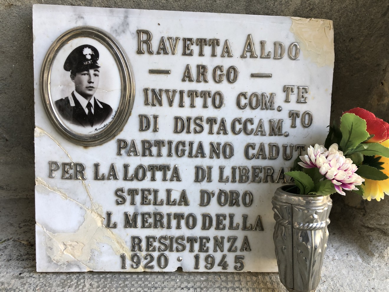 Targa commemorativa di Aldo Ravetta, partigiano caduto per la libertà, con foto e fiori in omaggio.