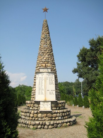 Monumento ai caduti di Castelletto Cervo, una stele a forma conica circondata da arbusti.