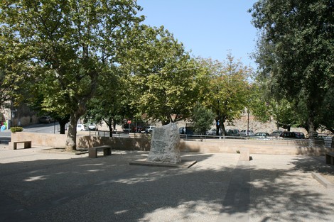 Monumento del ventennale immerso in un'area verde con alberi e panchine circostanti.