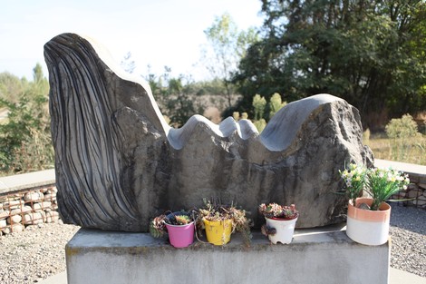 Scultura del "Monumento ai Martiri del Panaro" con piante decorative e un contesto naturale circostante.