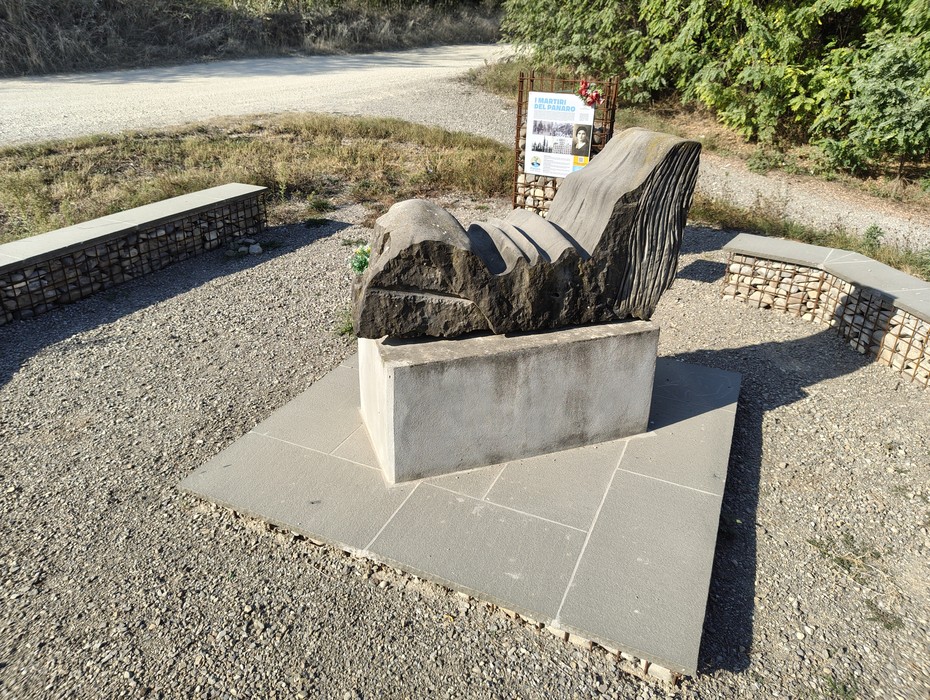 Monumento ai Martiri del Panaro, scultura su base di pietra con panchine intorno, immerso nella natura.