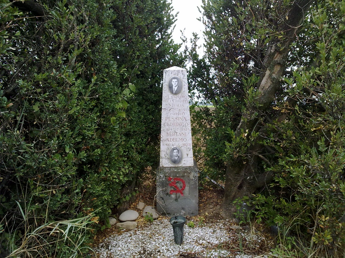 Cippo commemorativo dedicato a Pessina e Bertani, circondato da vegetazione.