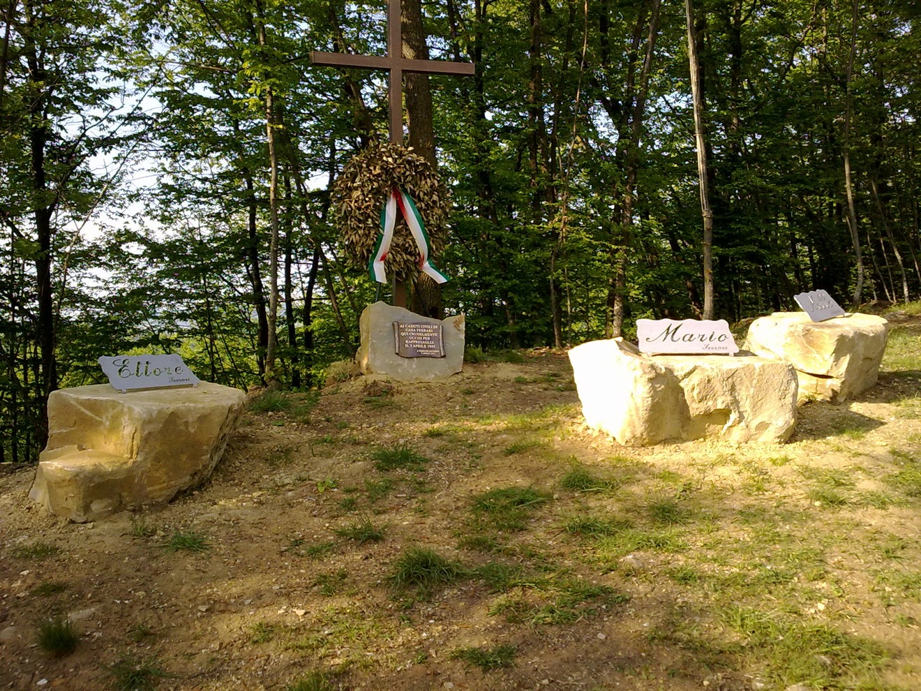 Monumento commemorativo ai Ferrari e Maroni, situato in un'area boschiva, con croce e targhe informative.