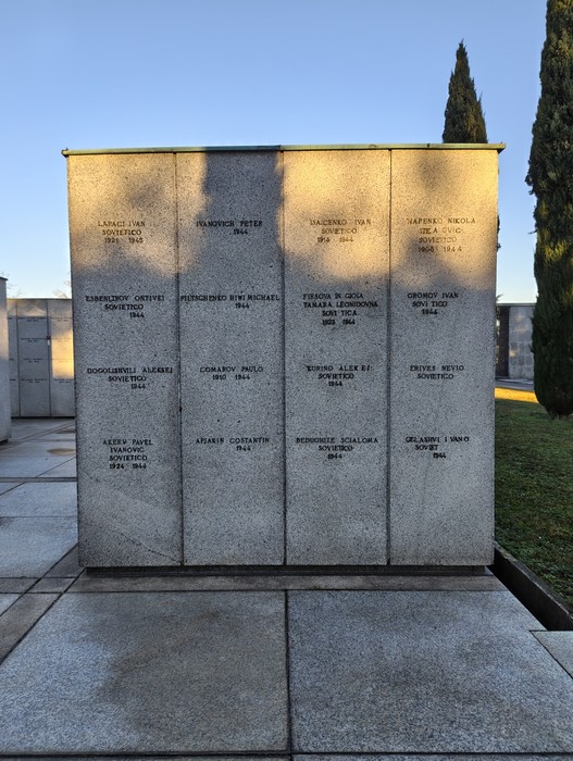 Monumento commemorativo al "Campo della Gloria" con lastre commemorative e cipressi sullo sfondo.