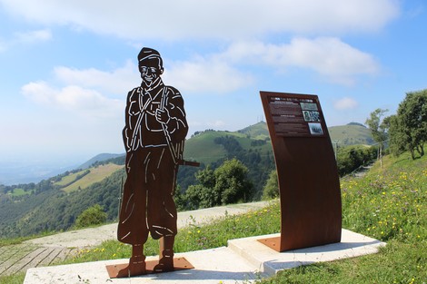 Scultura di un soldato e pannello informativo lungo la Strada della battaglia di Fonteno, circondata da colline verdi.