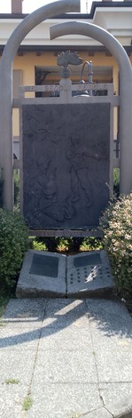 Monumento a D'Acquisto, con pannello in rilievo e decorazioni di bronzo, immerso nel verde.