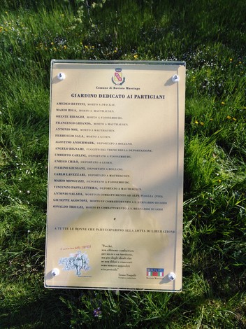 Targa commemorativa dedicata ai partigiani, posizionata nel giardino con fiori e verde circostante.