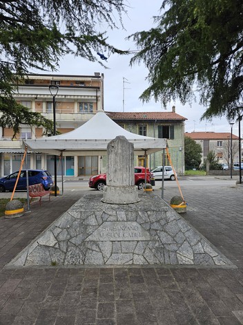 Monumento ai Caduti di Staranzano, situato in una piazza con alberi e edifici circostanti.