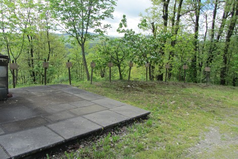 Monumento ai martiri dei Boschi di Ciano, circondato da alberi e oggetti commemorativi, in un ambiente naturale.