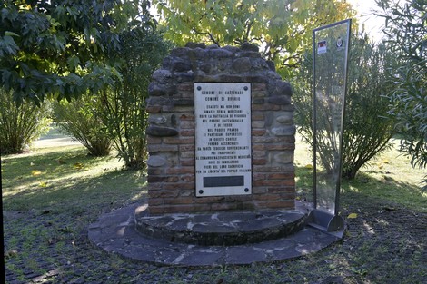 Monumento commemorativo alla battaglia di Casa Mengoli, circondato da vegetazione, con una lapide esplicativa.