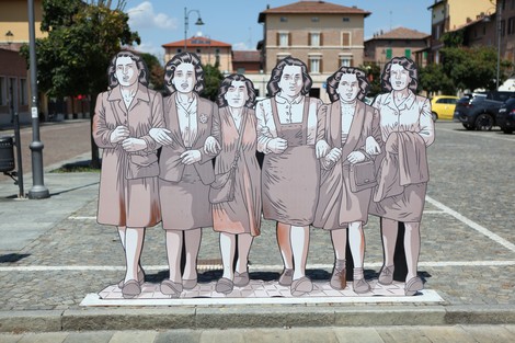 Scultura di otto donne in piedi, unite, con abiti storici, in un'ambientazione urbana luminosa.