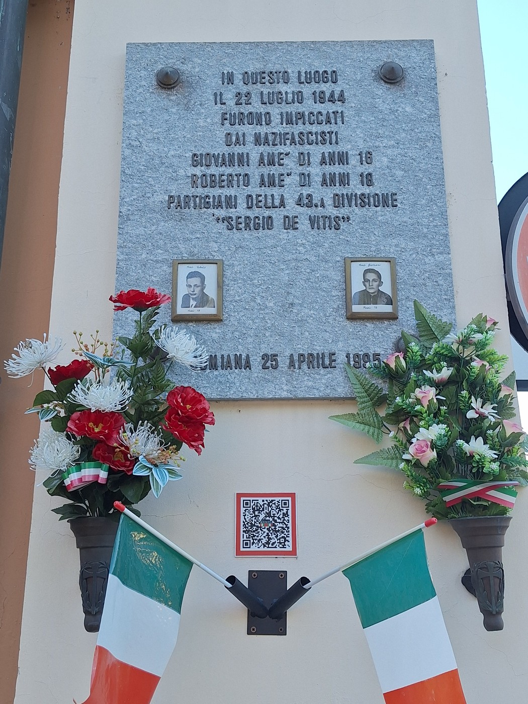 Lapide commemorativa dedicata ai fratelli Amè, con foto e decorazioni floreali.