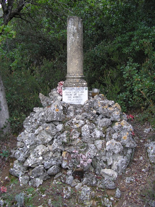 Cippo commemorativo a Giachi e Gamucci, circondato da pietre e vegetazione.
