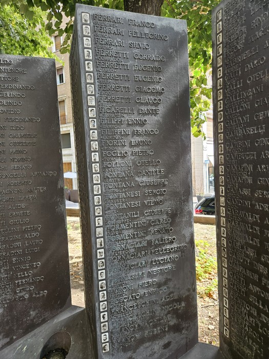 Pannello in pietra inciso con elenchi di nomi, parte del Sacrario della Resistenza Reggiana, in un’area alberata.