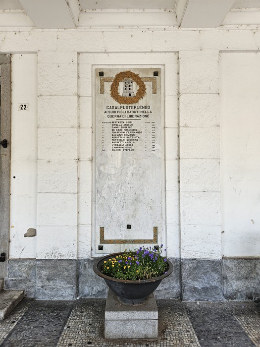 Lapide commemorativa ai caduti della guerra di Liberazione a Casalpusterlengo, con fiori decorativi.