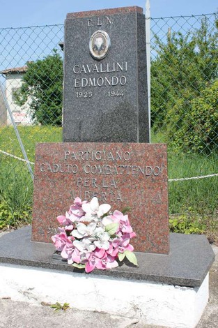 Cippo commemorativo dedicato a Edmondo Cavallini, partigiano caduto, con fiori davanti.