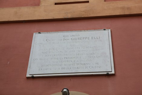 Lapide commemorativa dedicata a Don Giuseppe Elli, situata su una parete in un contesto architettonico.