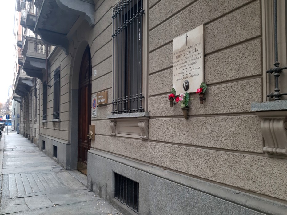 Lapide commemorativa di Caccia su una facciata di edificio urbano, decorata con un elemento floreale.