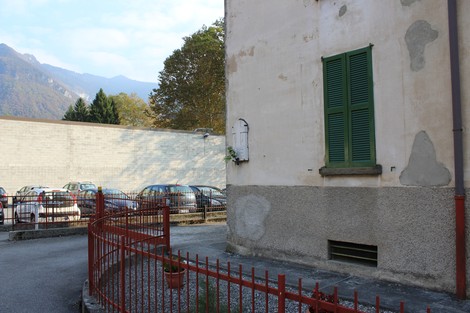 Lapide a Caccia e Carissimi su un muro, con auto parcheggiate e un albero in lontananza.