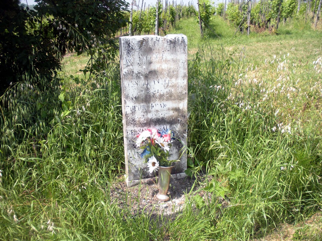 Lapide commemorativa della strage di Fontanone, adornata con fiori, immersa nella natura circostante.