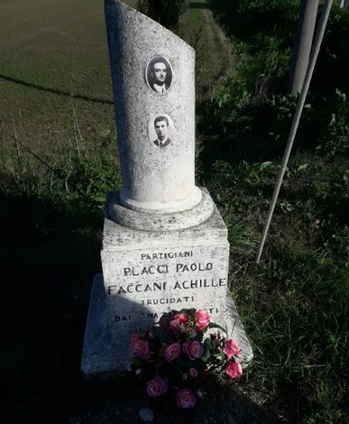 Cippo commemorativo dedicato ai partigiani Placci e Faccani, decorato con fiori e foto, in un contesto rurale.