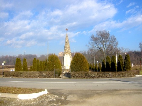 Monumento ai caduti di Castelletto Cervo, con alberi e cielo azzurro sullo sfondo.