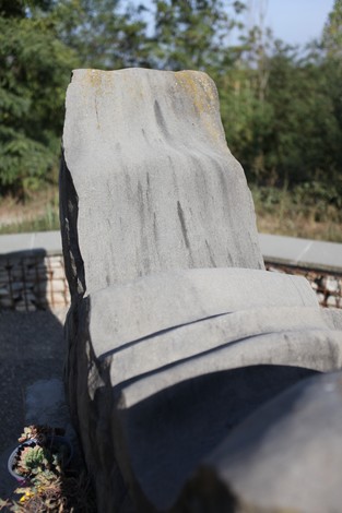 Monumento ai Martiri del Panaro, scultura in pietra con linee sinuose, circondato da verde. Atmosfera di rispetto e memoria.